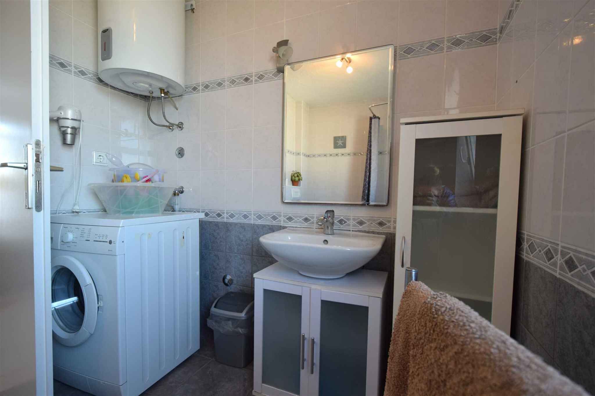 Ein kleines Badezimmer mit Waschmaschine, Waschbecken, Spiegel und Duschkabine.