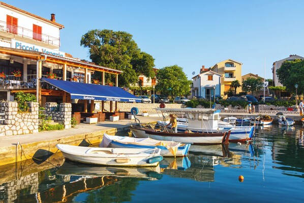 A waterfront restaurant with outdoor seating, boats docked in the background, and a clear sky. - Studio with air conditioning close to the beach (Vantačići)