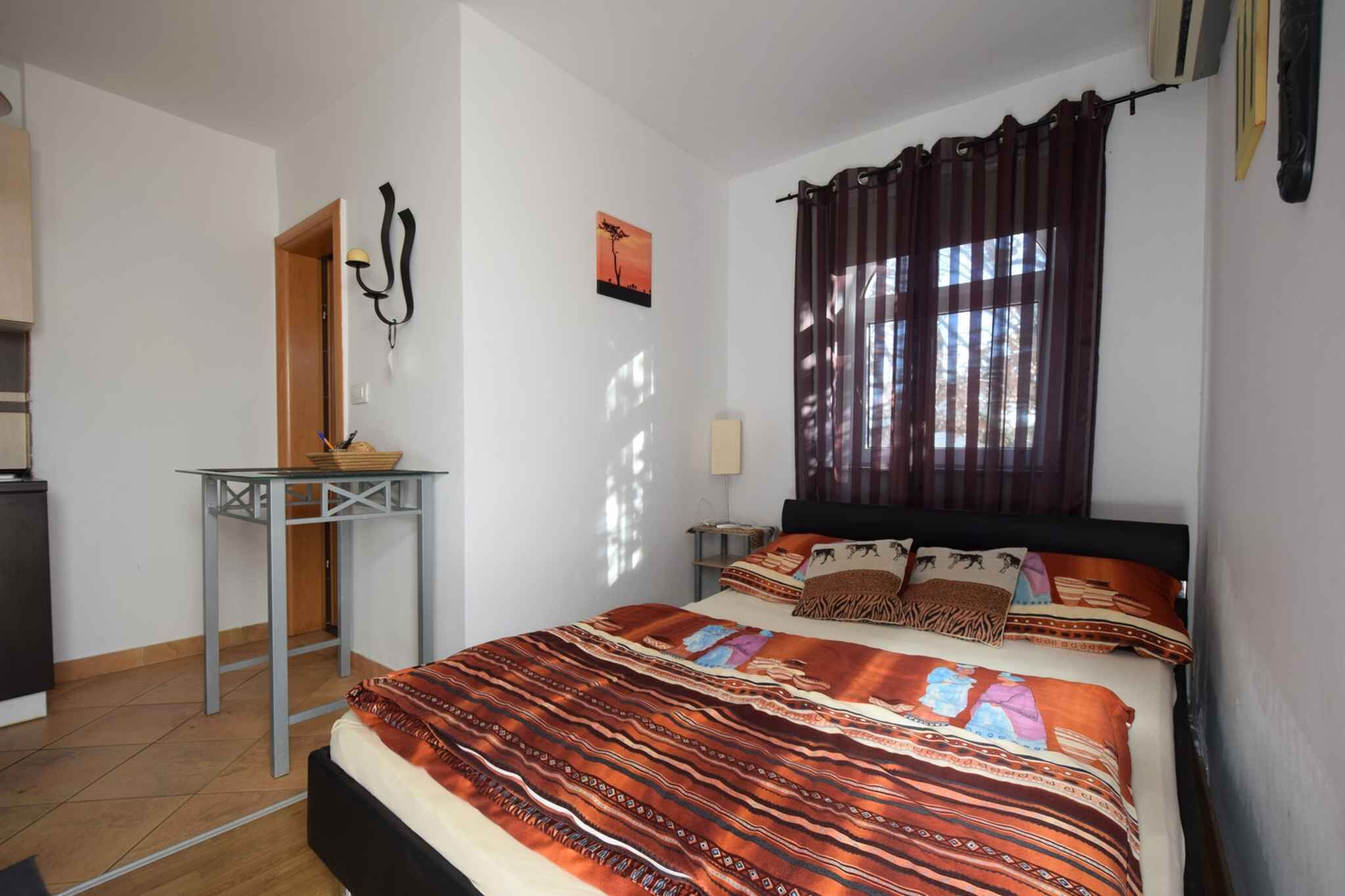A bedroom with a bed, a small table, a nightstand, a lamp, and a window with curtains.