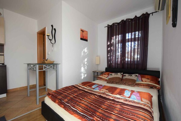 Un dormitorio con cama, una mesita, una mesita de noche, una lámpara y una ventana con cortinas.