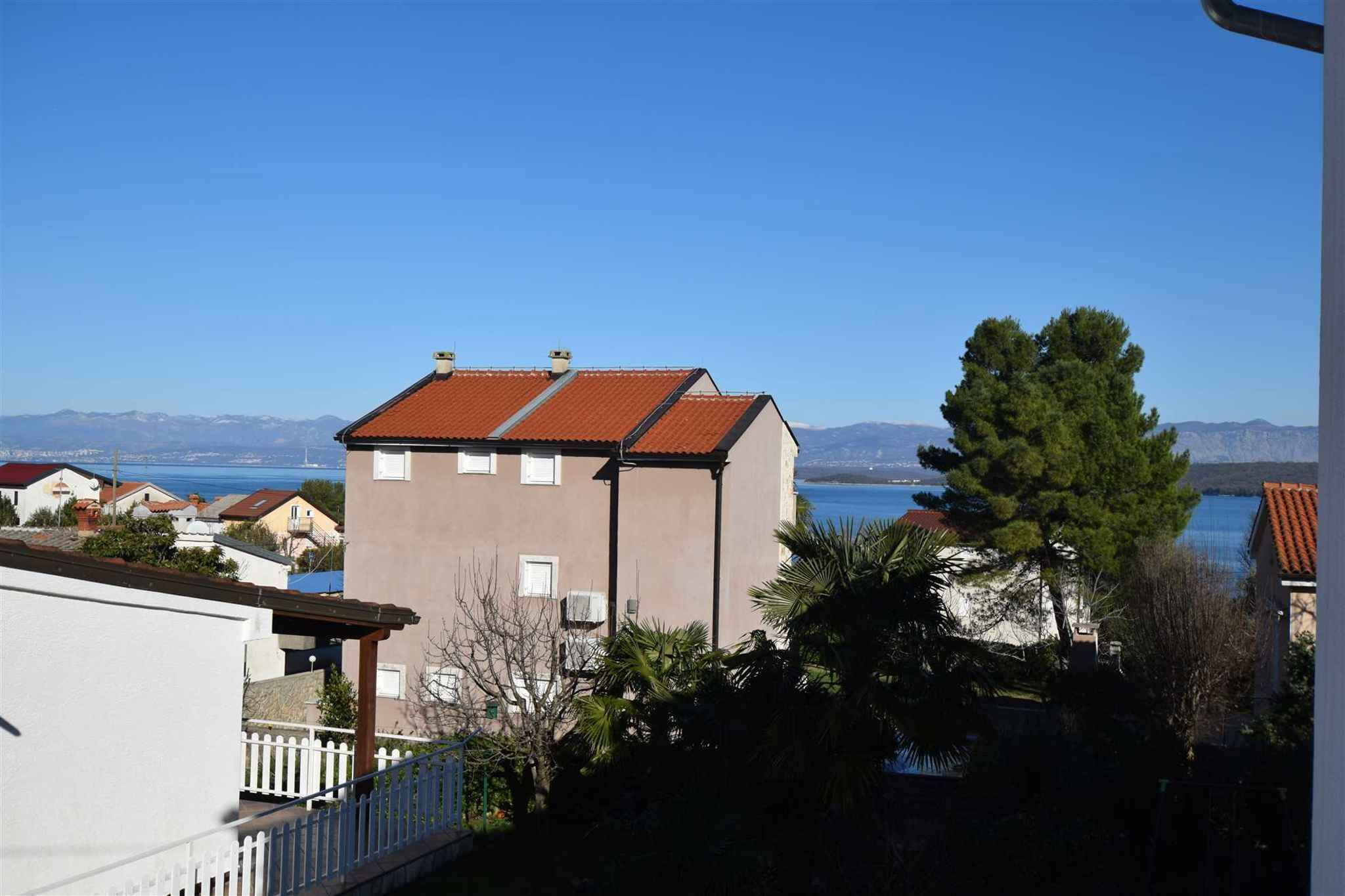 A building with a red roof, a balcony, and a view of a body of water and mountains.