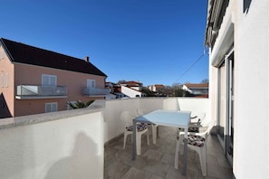 Un balcon avec une table et des chaises, un mur blanc et les bâtiments voisins.