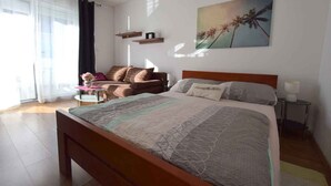 Un dormitorio con cama, sofá, una mesita, lámpara y un cuadro en la pared.