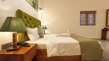 Una cama bien hecha con un cabecero verde, una lámpara de noche y una toalla con forma de cisne.