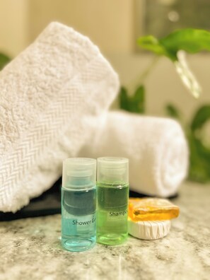 Two bottles labeled 'Shower Gel' and 'Shampoo' on a marble countertop with a white towel and a yellow soap bar.