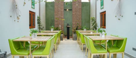 A dining area with multiple tables and green chairs, a brick wall, and decorative plants.