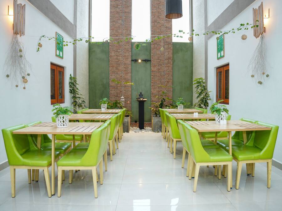 A dining area with multiple tables and green chairs, a brick wall, and decorative plants.