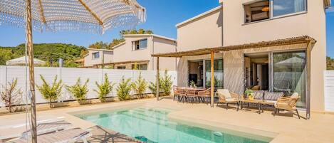 Uma casa moderna com piscina, mobiliário de exterior e uma pérgula.