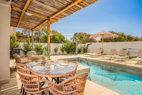 A poolside area with a table set for dining, lounge chairs, and a covered seating area.