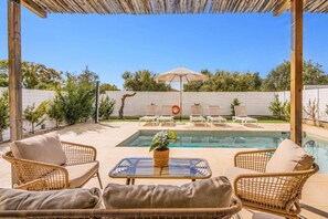 A pool area with lounge chairs, a table, and a pergola.