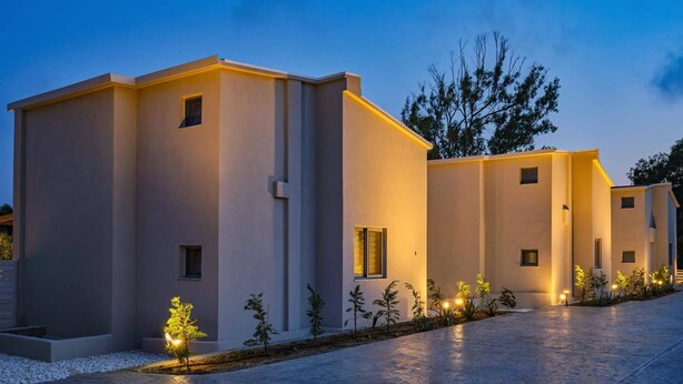 A modern building with a symmetrical facade, multiple windows, and a pathway lined with small trees and lights.