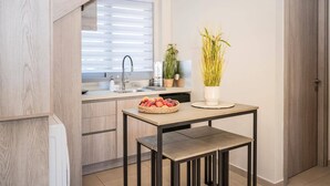 A modern kitchen with a built-in oven, a sink, and a window with blinds. There is a table with a bowl of fruit and a potted plant.