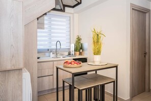 A modern kitchen with a built-in oven, a sink, and a window with blinds. There is a table with a bowl of fruit and a potted plant.