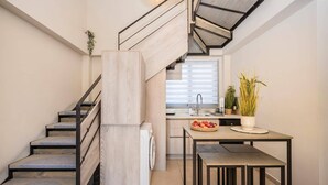A modern kitchen with a built-in staircase, a dining area with a table and chairs, and a window with blinds.