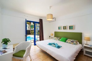 A hotel room with a bed, a chair, a desk, a lamp, and a view of an outdoor pool.