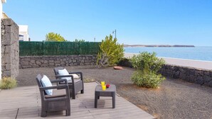 Eine Terrasse mit Korbmöbeln, einem kleinen Tisch mit Getränken und Blick aufs Meer.