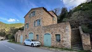 Un bâtiment en pierre avec une voiture garée devant, un escalier et une colline en arrière-plan.