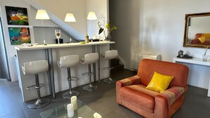 Un salon moderne comprenant un canapé, une table basse et un coin bar avec des tabourets.
