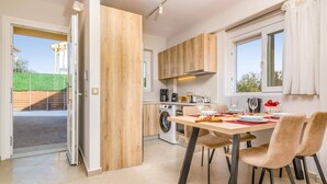 A modern kitchen with wooden cabinets, a dining table with chairs, a washing machine, and a window with curtains.