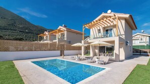 A modern villa with a swimming pool, outdoor seating, and a mountain backdrop.
