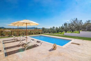 Piscina retangular com área de descanso, incluindo espreguiçadeiras e uma mesa com guarda-sol.
