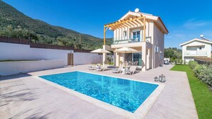 Et moderne hus med to etager, en swimmingpool, udendørs siddepladser og udsigt over et kuperet landskab.