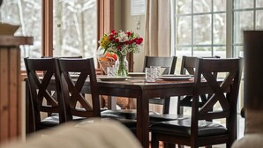 Une table à manger avec quatre chaises, un vase rempli de fleurs et une fenêtre donnant sur des arbres.