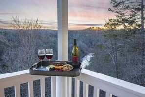 En balkon med et bakkesæt, der indeholder to glas rødvin, en vinflaske og en tallerken med snacks.