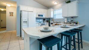 Une cuisine moderne avec des meubles blancs, un grand îlot central doté de tabourets et un four à micro-ondes encastré.