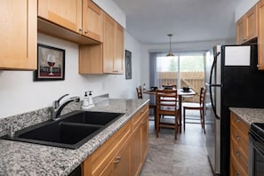 A kitchen with granite countertops, wooden cabinets, a black sink, and a refrigerator.