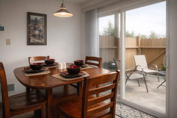 A dining area with a wooden table, six chairs, and red bowls. There is a window with a view of a wooden fence and chairs outside.
