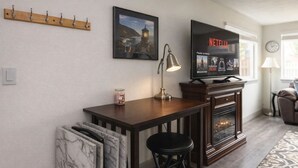 Een woonkamer met een open haard, een televisie waarop 'Netflix' wordt weergegeven, een lamp, een fotolijstje en een kapstok.