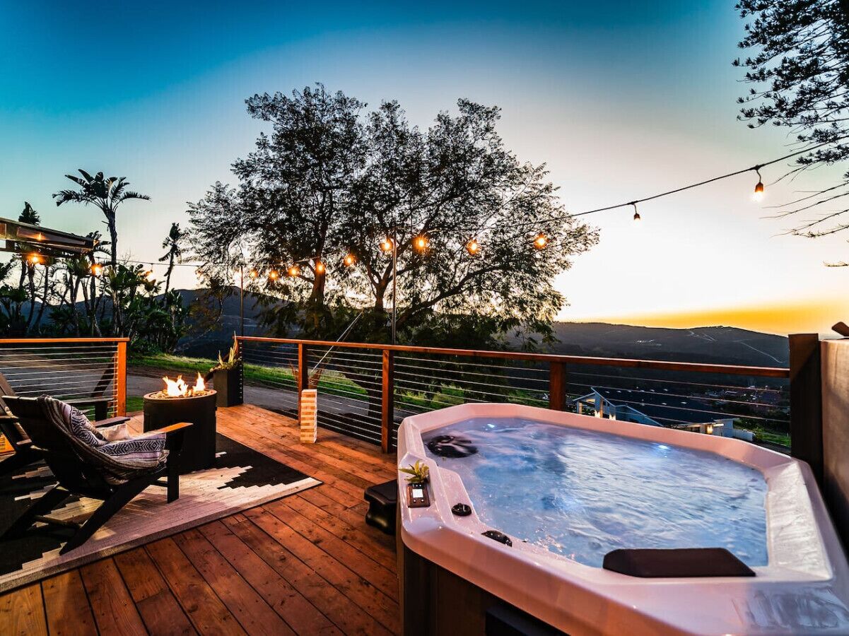 A wooden deck with a hot tub, lounge chairs, and string lights.