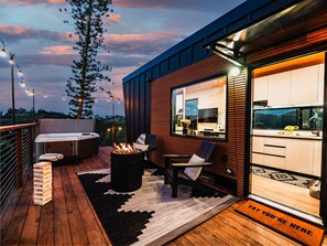 A modern outdoor deck with a hot tub, seating area, and a view of the kitchen.
