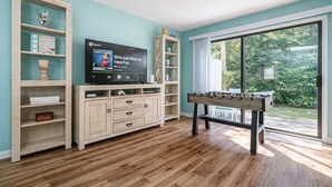 A living room with a foosball table, a flat-screen TV, and a bookshelf. - Summer Escape | Walk to Private Beach | Pets OK (Destin)