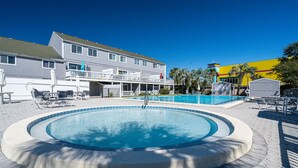 A swimming pool with a circular design, surrounded by lounge chairs and a building with a balcony. - Summer Escape | Walk to Private Beach | Pets OK (Destin)
