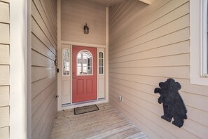 Ein Haus mit roter Tür, einer kleinen Veranda und einer Bär-förmigen Dekoration an der Wand.