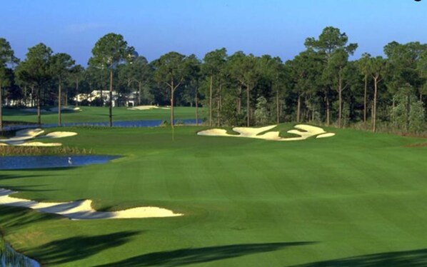 A golf course with sand bunkers, water hazards, and a clear sky.