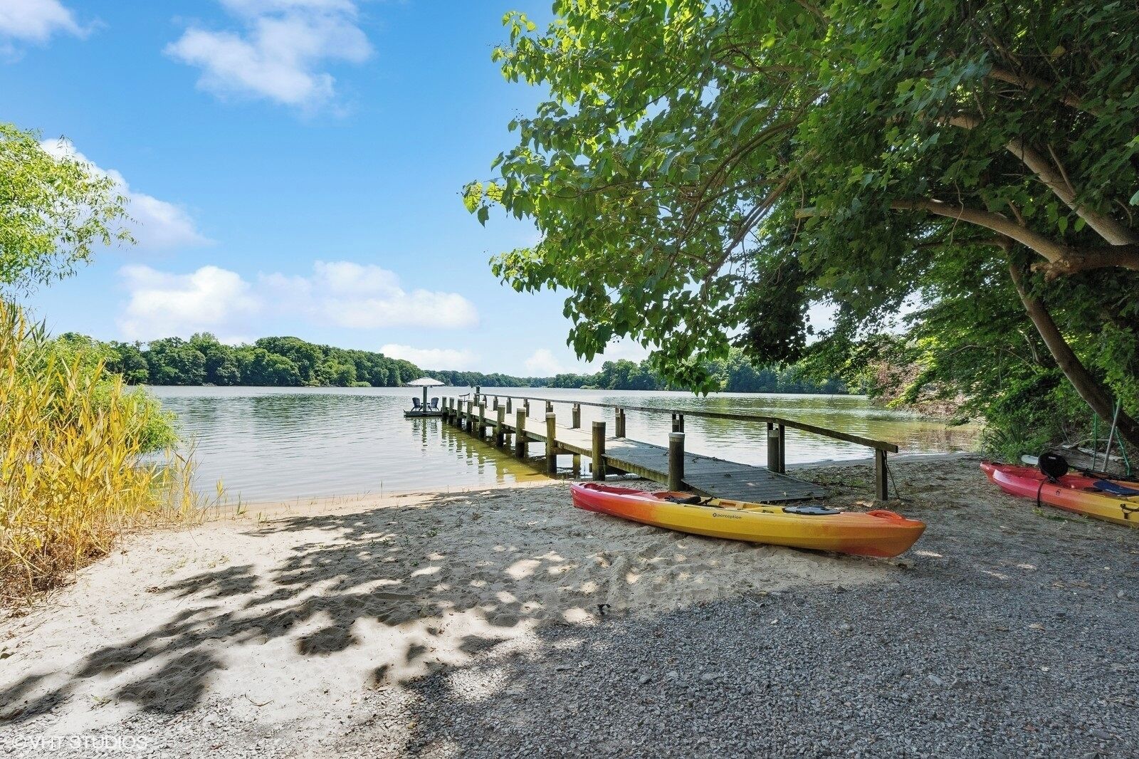 A gravel dock extending into a calm lake, surrounded by trees and greenery.