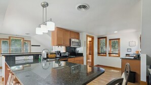 Una cocina moderna con encimeras de granito, armarios de madera, microondas integrado y una isla grande con un lavamanos.