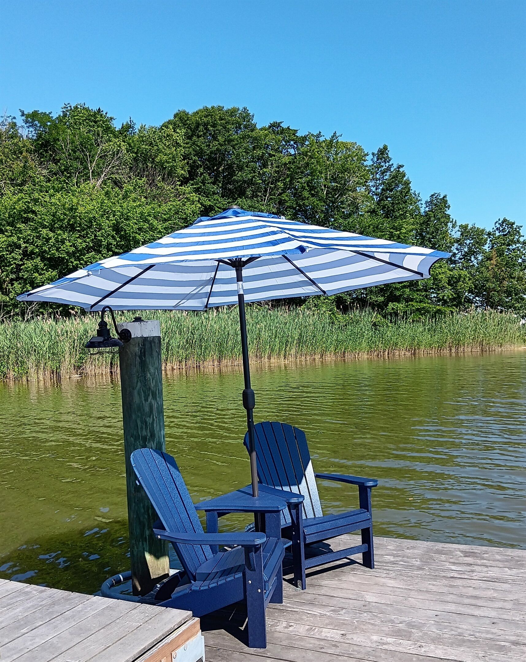 Un muelle con dos sillas Adirondack y una sombrilla a rayas.