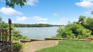 A lakeside deck with a wooden railing, a lamp post, and a grassy area leading to the water. - Waterfront Retreat with Private Dock and Beach (Worton)