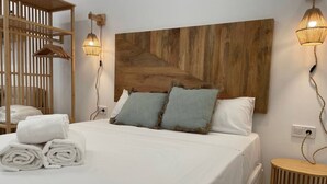 A neatly made bed with white linens and two pillows, a wooden headboard with a geometric pattern, and two wall-mounted lamps.