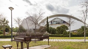 An outdoor seating area with a metal sculpture and a bench, in front of a modern building with a curved roof.
