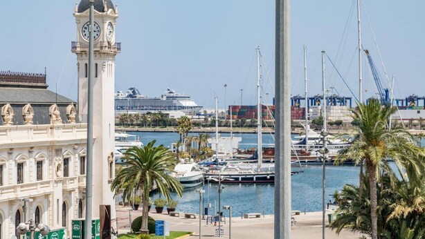 A coastal marina with a prominent clock tower, yachts, and a cruise ship in the background.