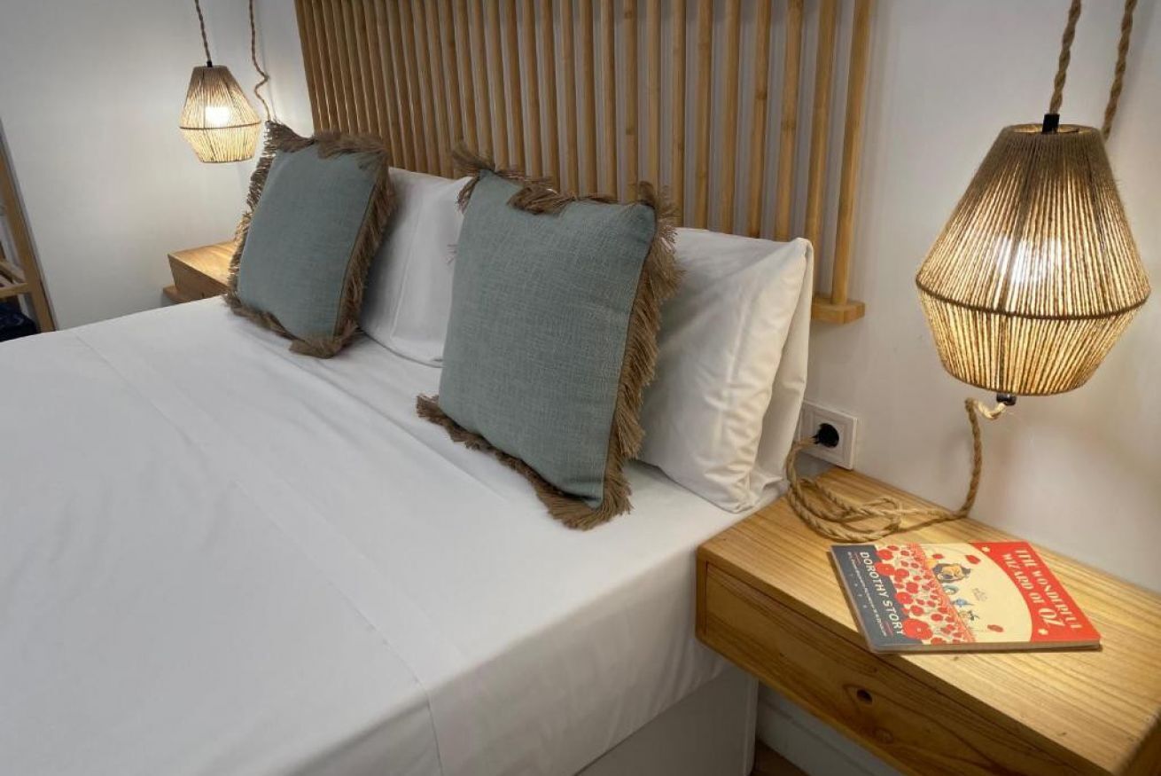 A neatly made bed with two pillows, a bedside table with a book, and two hanging lamps.