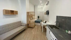 A compact living space with a sofa, a small dining area, a kitchenette, and a wooden partition. - Travel Habitat Cabanyal Loft 3 (Valencia / València)