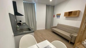 A modern living room with a sofa, a dining table with a laptop, and a kitchen area with a sink and stove. - Travel Habitat Cabanyal Loft 3 (Valencia / València)