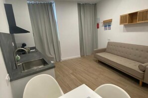 A modern kitchenette with a sink and countertop, a beige sofa, and a dining table with chairs. - Travel Habitat Cabanyal Loft 3 (Valencia / València)