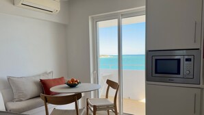 Eine moderne Küche mit Mikrowelle, einem Esstisch mit Stühlen, einer Couch und Meerblick durch eine Glastür.